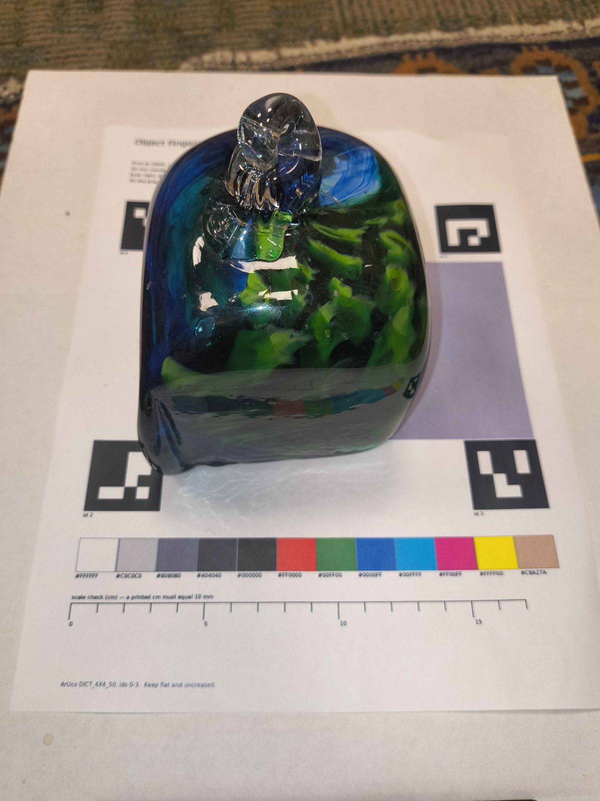 A blue and green glass paperweight on the printed ArUco and colour-checker mat.